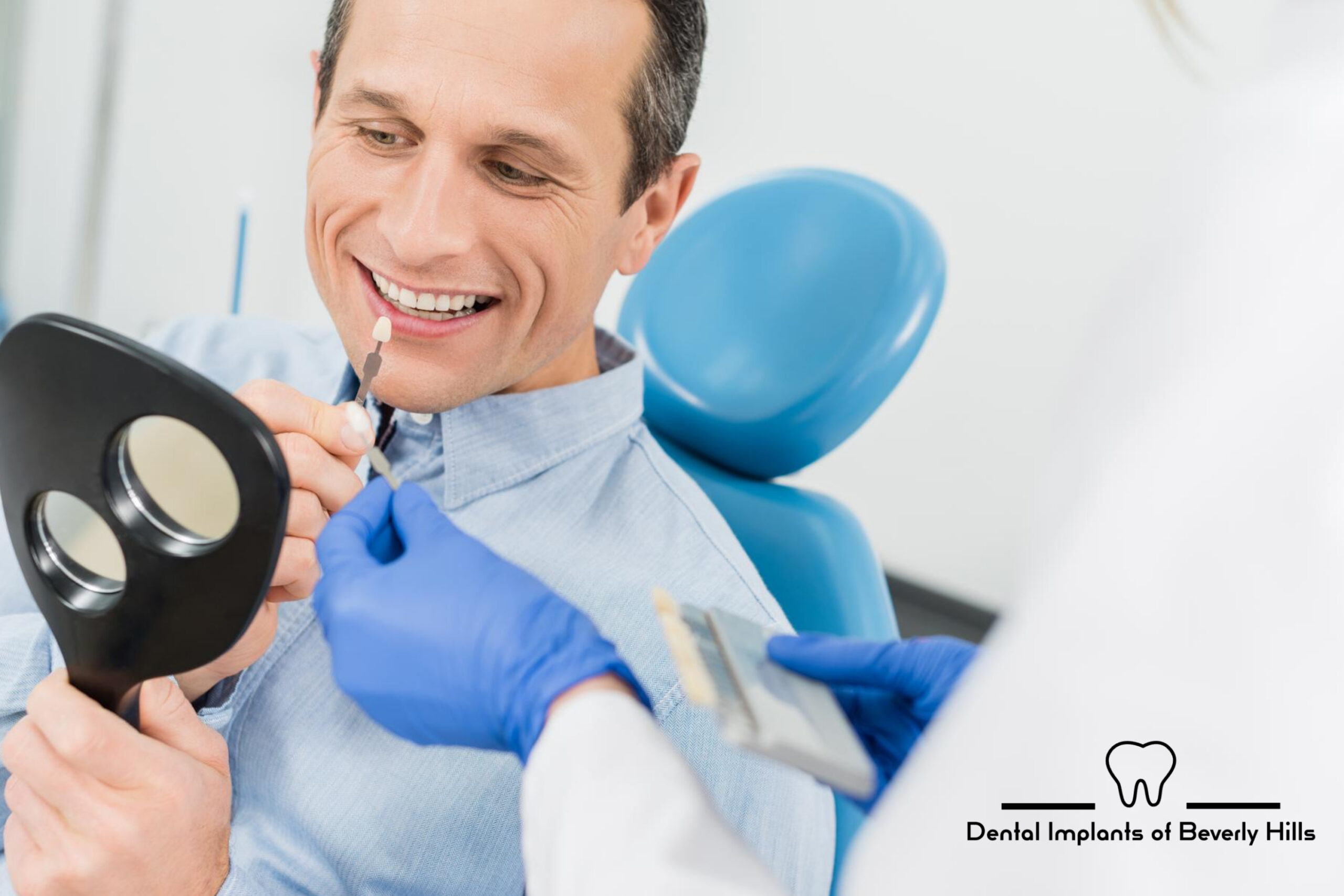 Man matching affordable dental implant color options to his teeth in mirror by his dentist